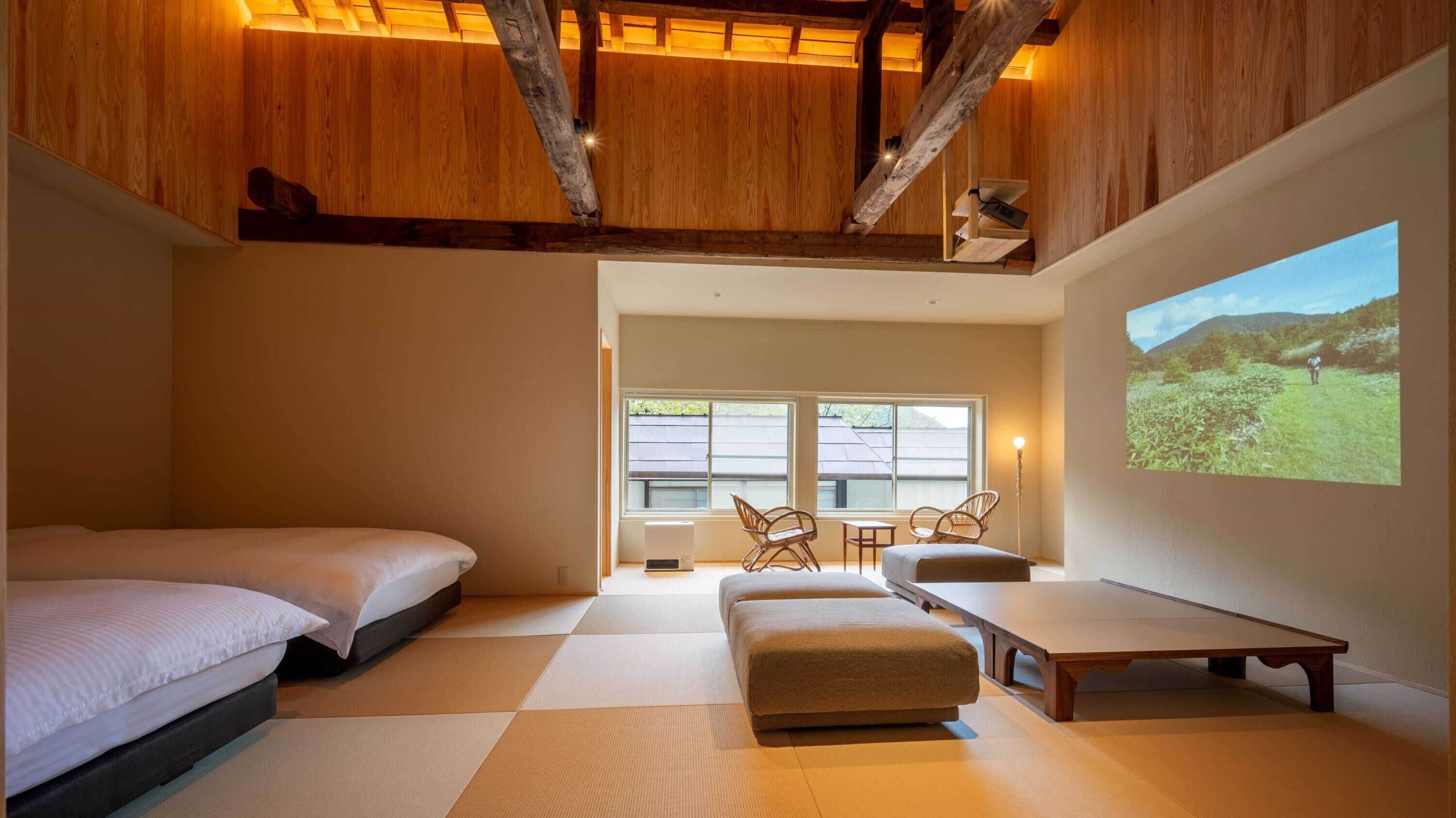 Un dormitorio con cama, sofá, mesa y pantalla de proyector mostrando un paisaje.