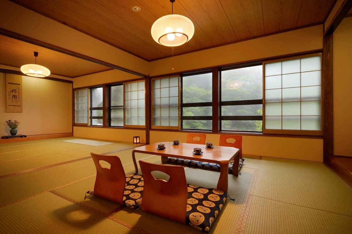 Una habitación japonesa tradicional con suelo de tatami, una mesa baja con cojines, puertas correderas y un televisor.