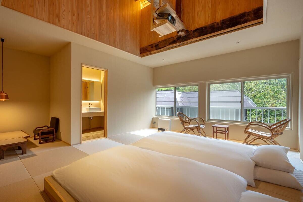 A bedroom with a large bed, a bedside table, a chair, a small table, and a window with a view.