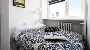 A bedroom with a bed, a window with a view of buildings, a radiator, and a painting on the wall. - Elegant Apartment Panoramic (Warsaw)