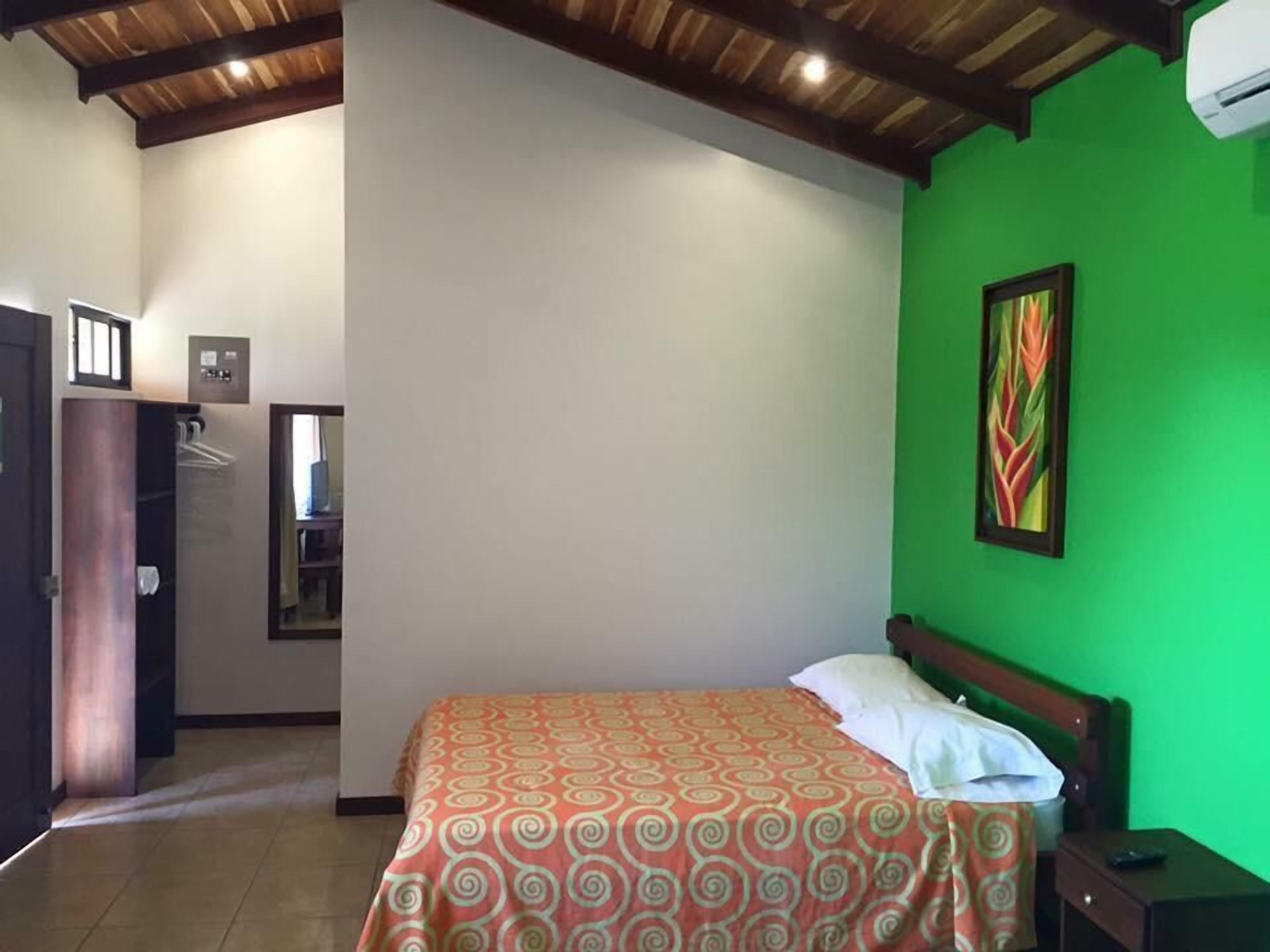 Un dormitorio con una cama, pared verde, un cuadro y techo de madera.