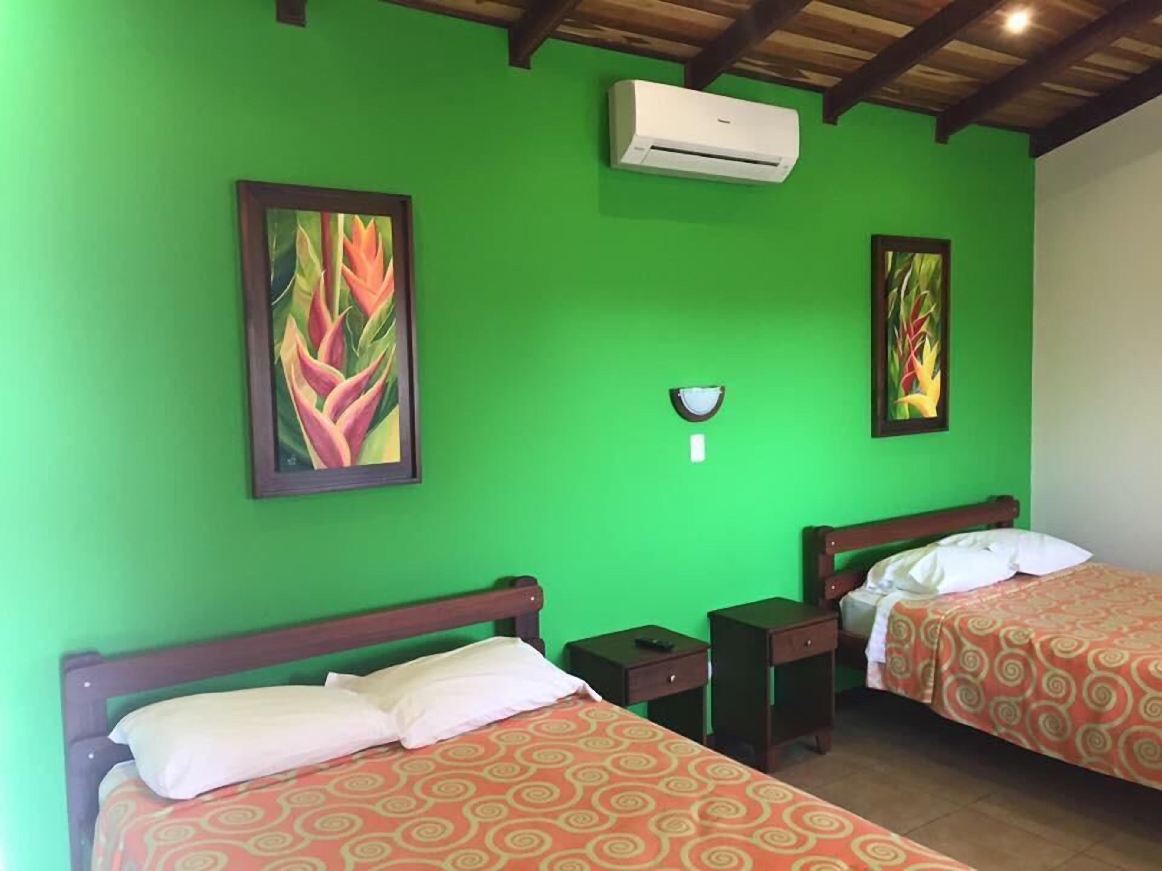 Une chambre avec deux lits, des murs verts et des poutres en bois au plafond.