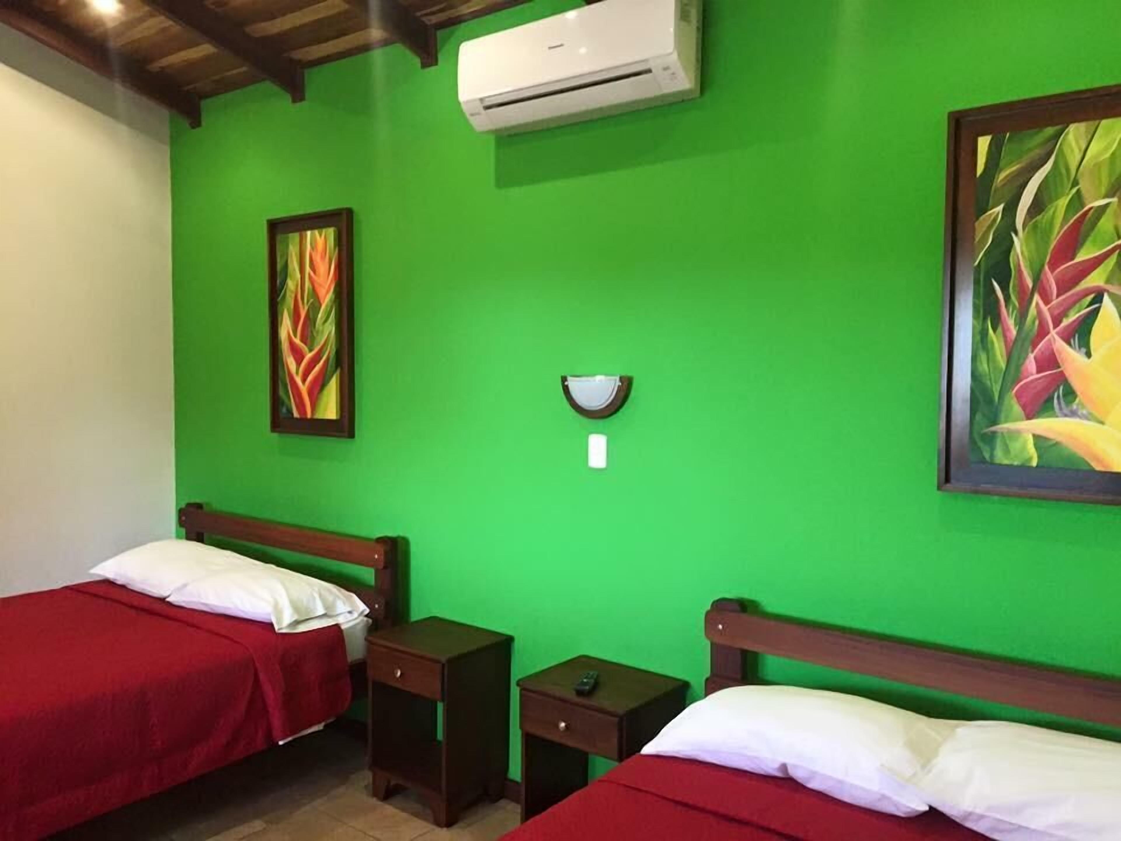 Quarto com duas camas, uma mesinha de cabeceira, ar condicionado fixado na parede e duas pinturas.