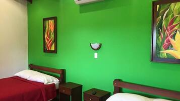 Quarto com duas camas, uma mesinha de cabeceira, ar condicionado fixado na parede e duas pinturas.