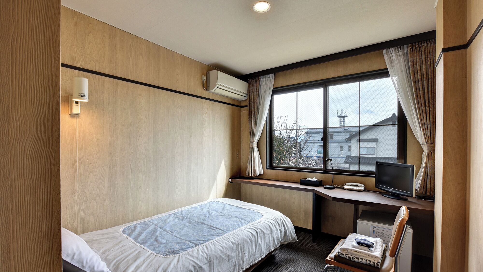 Ein Hotelzimmer mit Bett, Schreibtisch, Stuhl, Fernseher und einem fenster mit Vorhängen.