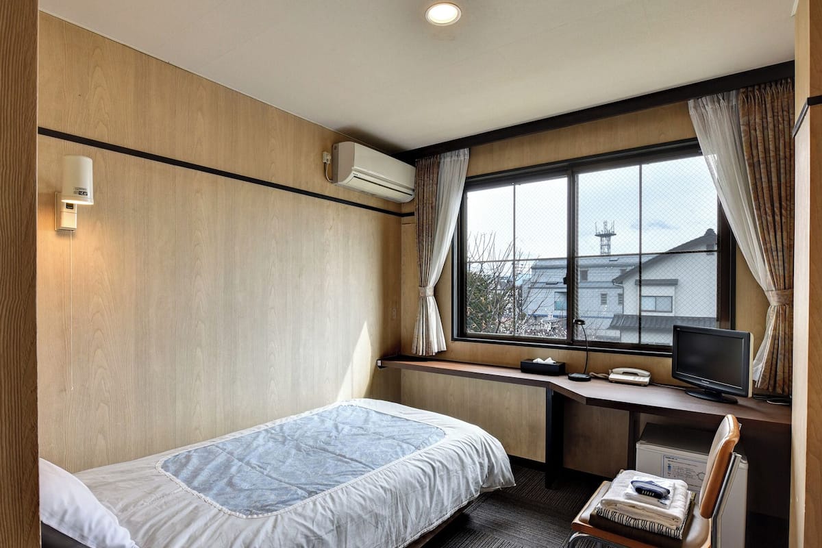 A hotel room with a bed, desk, chair, TV, and a window with curtains.