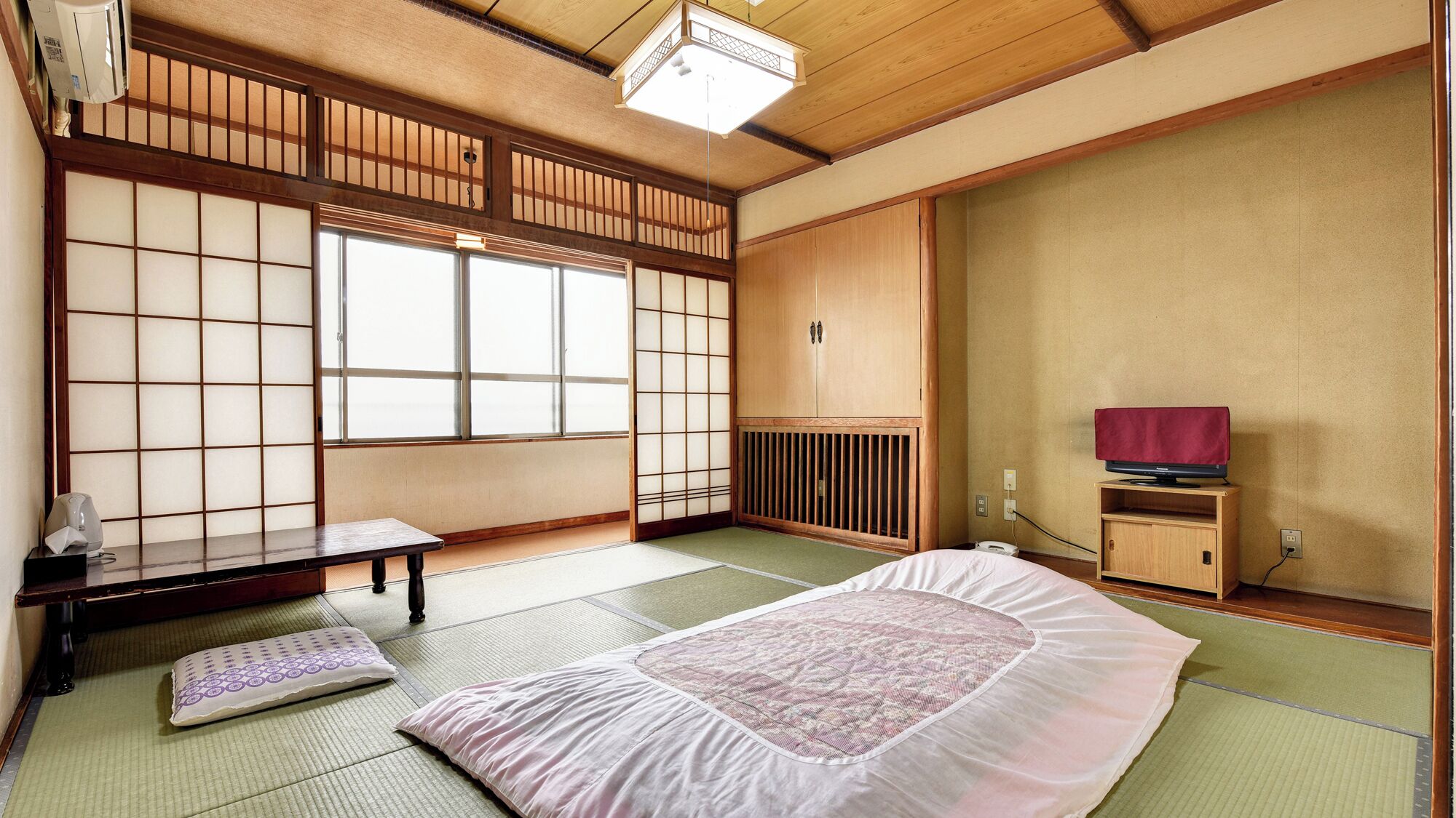 Ein traditioneller japanischer Raum mit Tatami-Bodenbelag, einem Futon, einem niedrigen Holzschrank und einer verschiebbaren Shoji-Schiebetür.