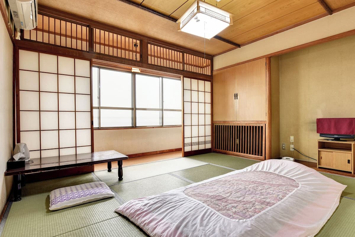 A traditional Japanese room with tatami flooring, a futon bed, a low wooden cabinet, and a sliding shoji screen door.
