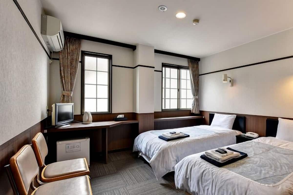A hotel room with two beds, a desk with a computer, a chair, and a window with curtains.