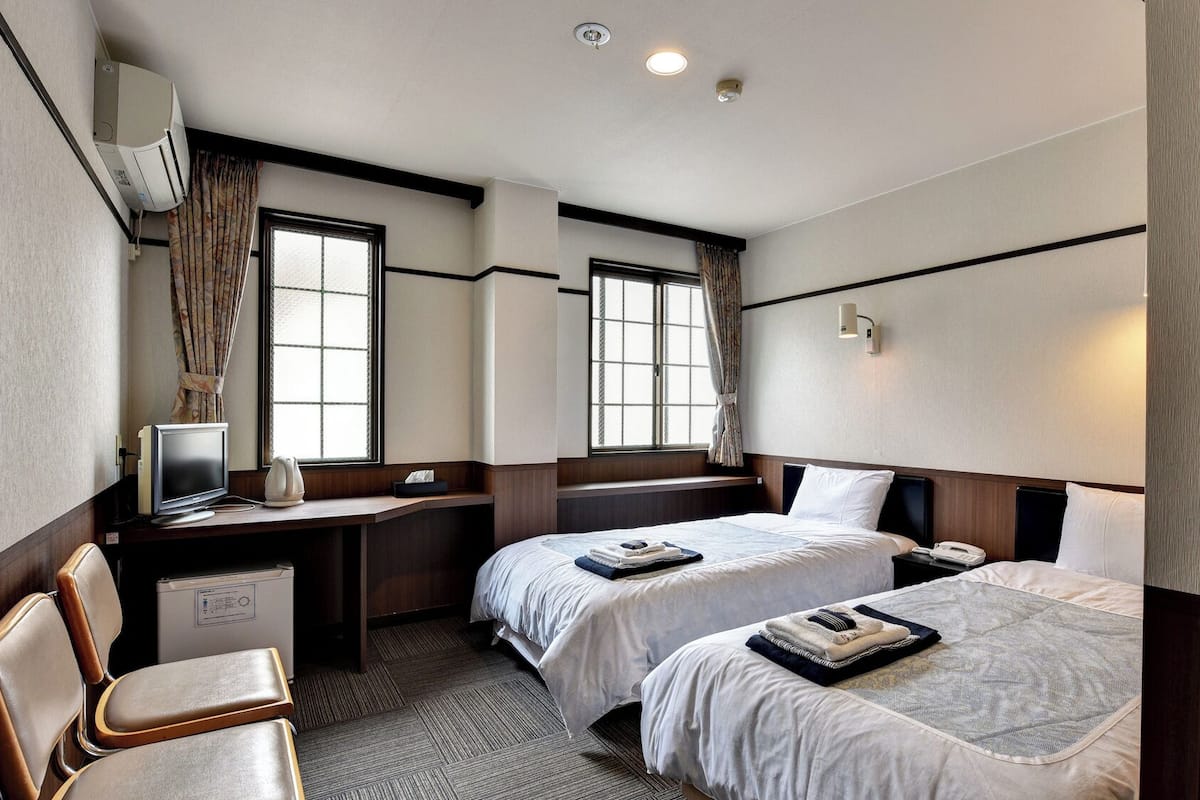 A hotel room with two beds, a desk with a computer, a chair, and a window.