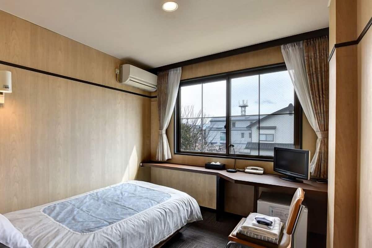 A hotel room with a bed, a desk with a computer, a chair, and a window with curtains.