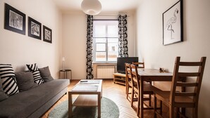 Una sala de estar moderna con un sofá, una mesa de centro, una mesa de comedor y sillas. Hay obras de arte enmarcadas en la pared, un televisor y una ventana con cortinas.