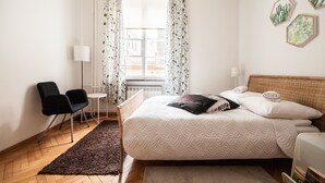Un dormitorio con cama, dos sillas, una mesita y una ventana con cortinas.