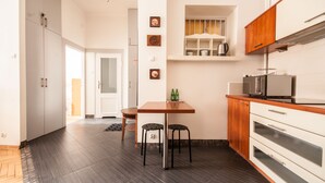 Una cocina moderna con suelo de madera oscura, armarios blancos y un microondas integrado. Hay dos taburetes junto a una mesa pequeña, y se ve un refrigerador al fondo.