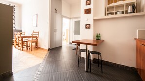 Una cocina moderna con una mesa y sillas de madera, una encimera con un hervidor y una estantería con tazas y una cafetera.