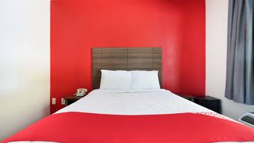 A hotel room with a red accent wall, a white bedspread, and a grey curtain.