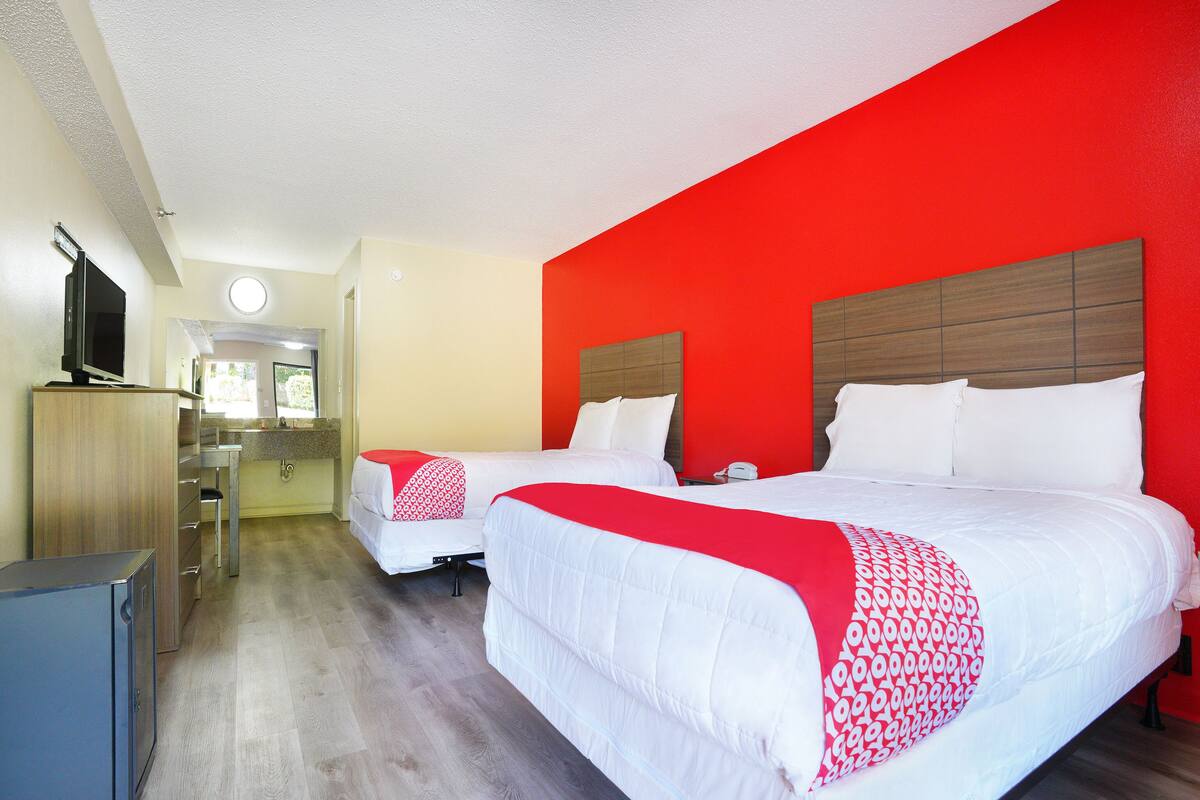 A hotel room with two beds, a TV, a desk, and a bathroom visible in the background.