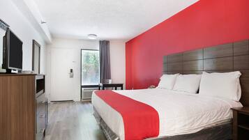 A hotel room with a bed, a desk, a television, and a window with curtains.