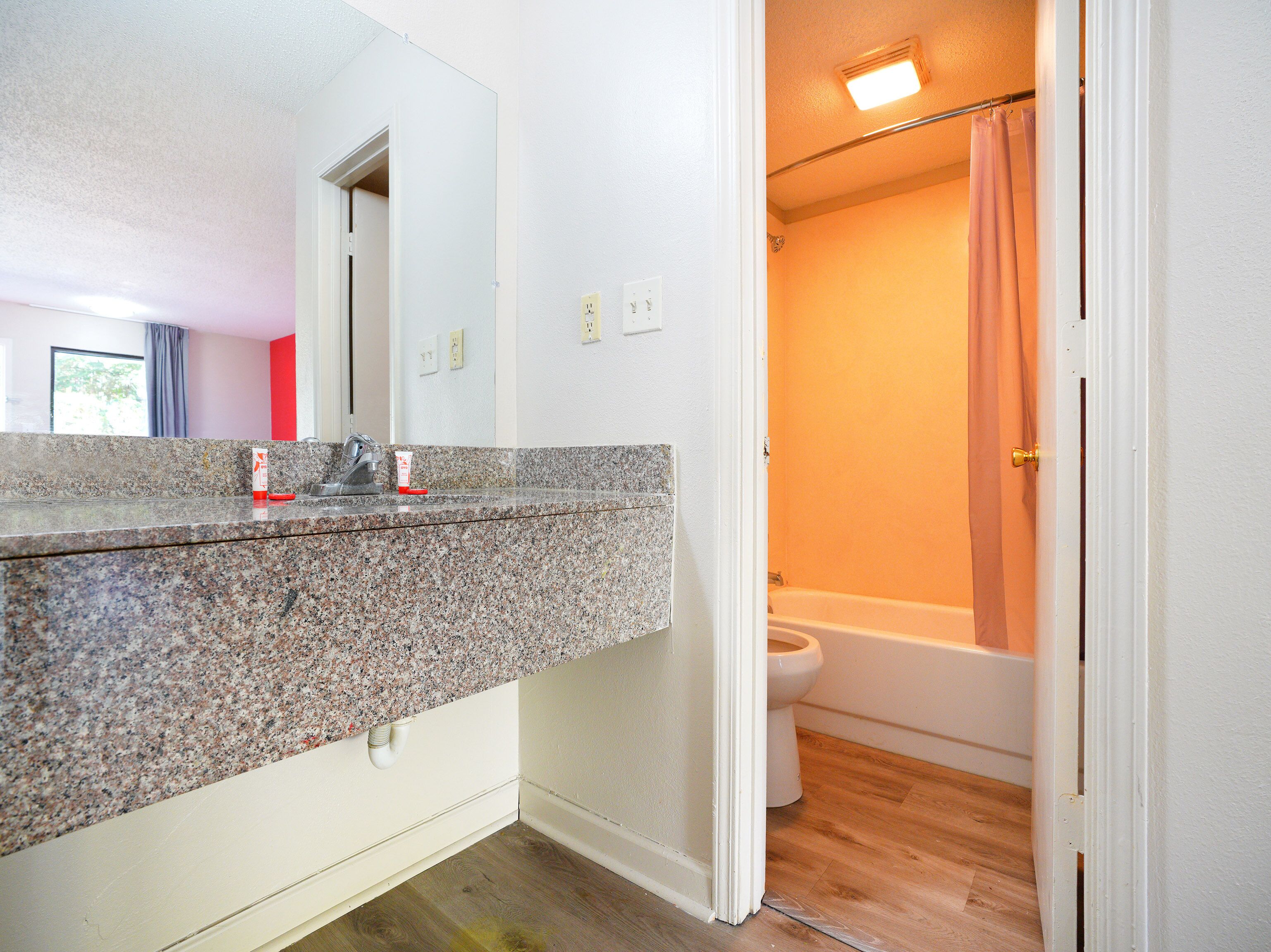 A bathroom with a granite countertop, a white toilet, and a shower with a curtain.