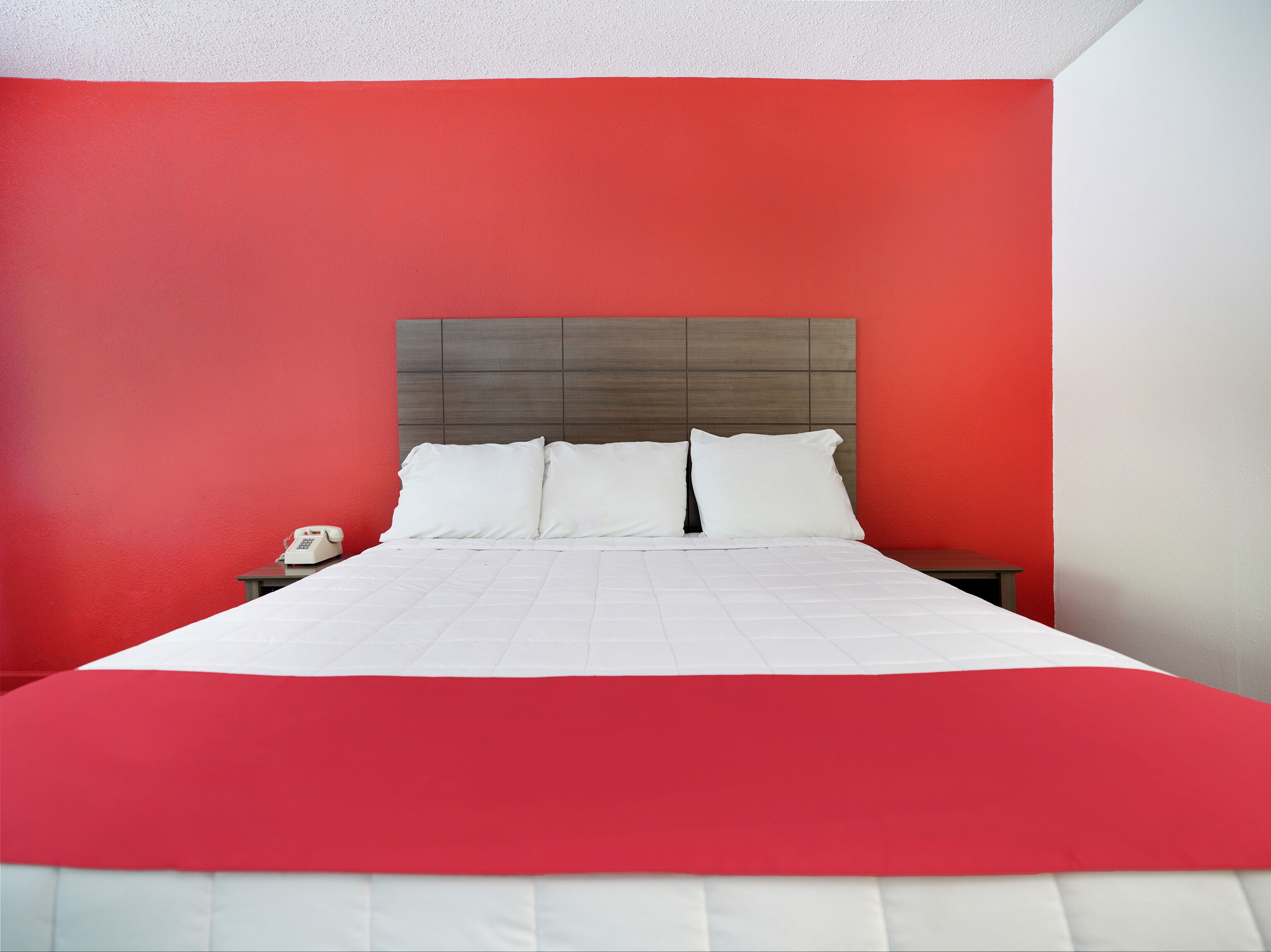 Un lit avec une literie blanche et un mur d’accent rouge.