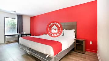 Een schone, moderne slaapkamer met een rode accentmuur, een net opgemaakt bed, een klein nachtkastje en een raam met gordijnen.