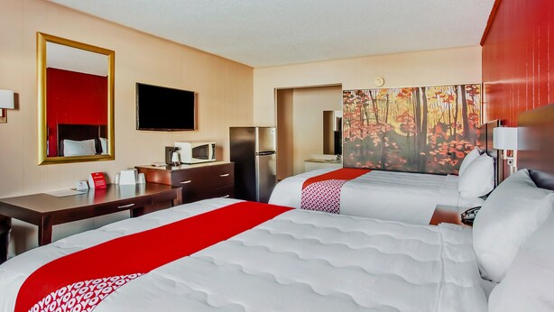 A hotel room with two beds, a desk, a TV, a microwave, and a painting on the wall. - OYO Hotel Ridgeland East (Ridgeland)