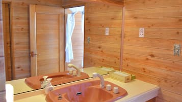 A bathroom with wooden panel walls, a pink sink with a mirror, and a window with curtains.