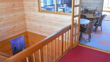 A wooden interior with a dining area, a staircase, and a view through a window.