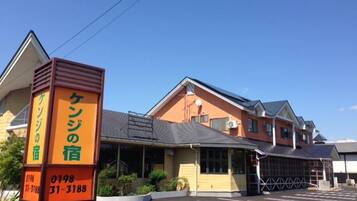 A hotel with a parking lot, a signboard with contact information, and a building with a sloped roof.