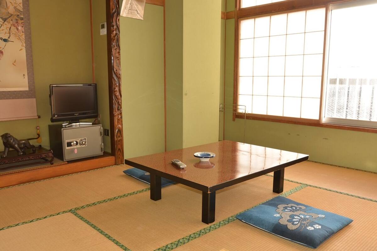 Une pièce de style japonais traditionnel, avec un sol recouvert de tatamis, une table basse, un téléviseur et un coffre-fort.