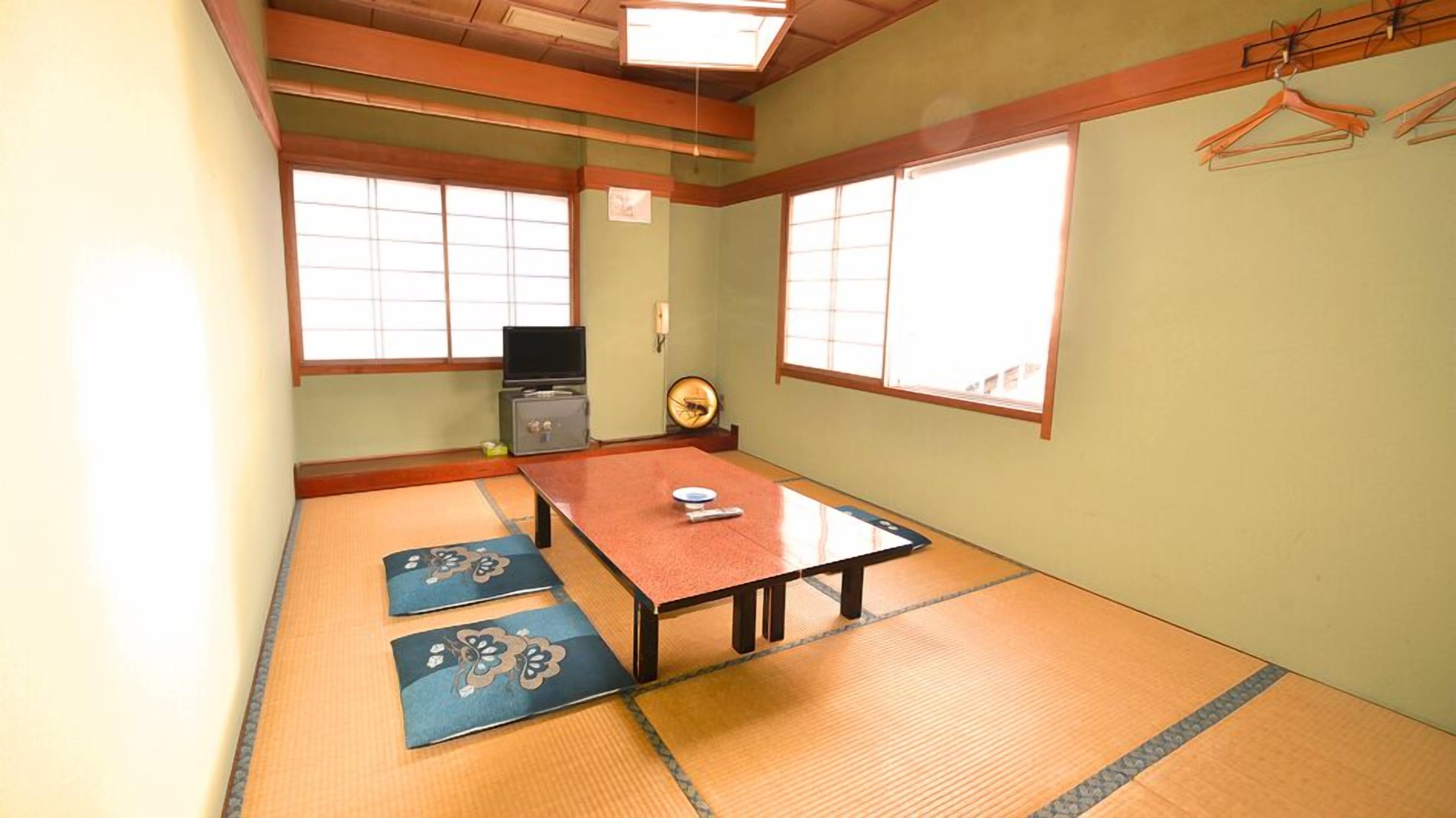 Ein Raum mit Tatami-Matten, einem niedrigen Tisch, einem Fernseher und einem Schrank.