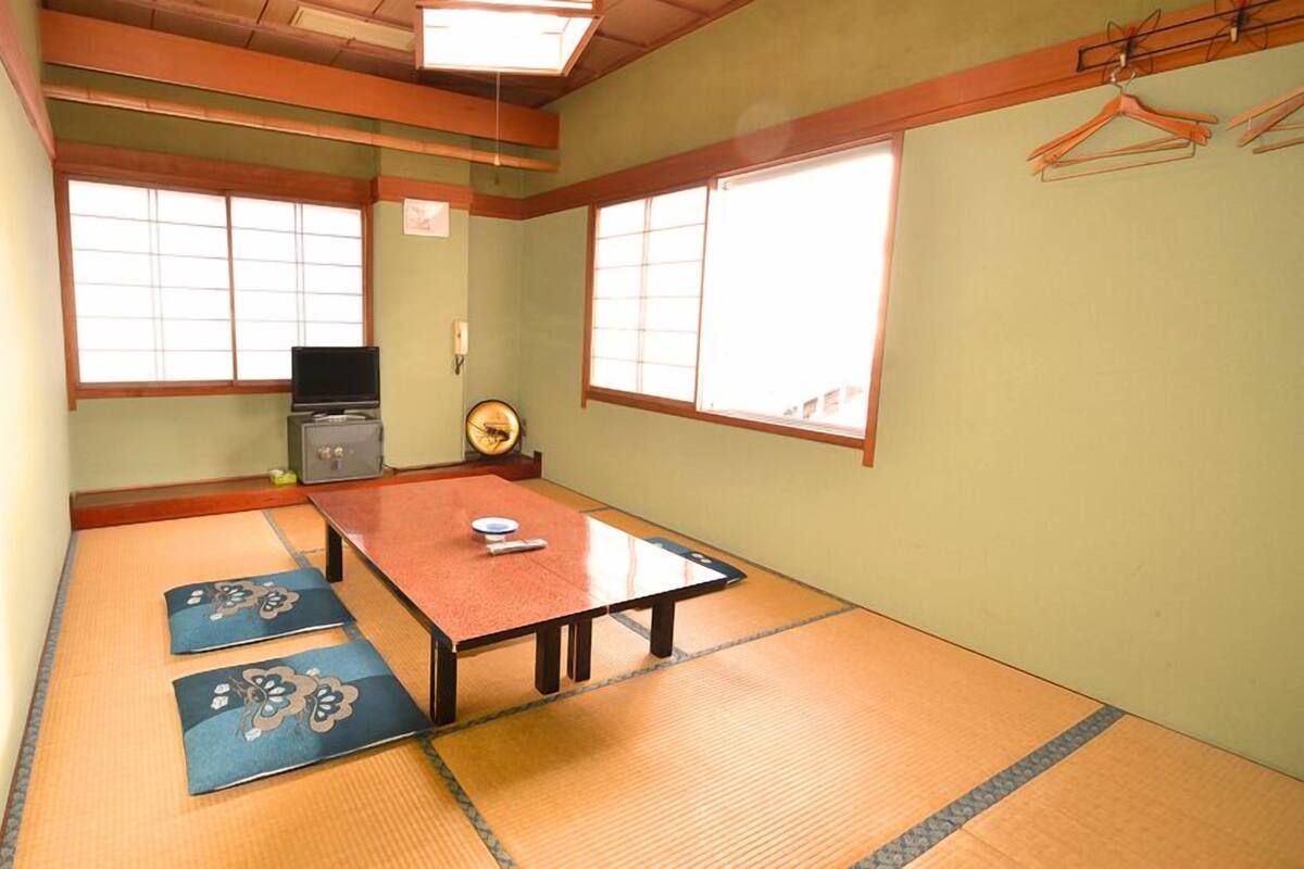 Une pièce avec un sol recouvert de tatamis, une petite table basse, un téléviseur et un meuble.