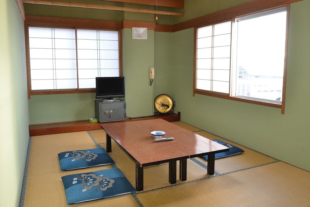 Une pièce avec un sol recouvert de tatamis, une petite table, un téléviseur et un objet décoratif accroché au mur.