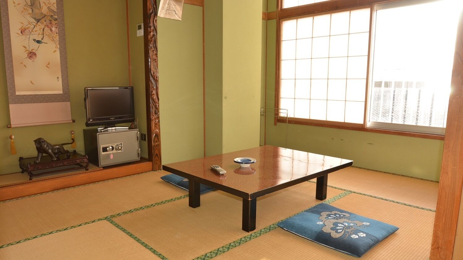 Ein Raum mit Tatami-Matten, einem niedrigen Tisch, einem Fernseher und einer dekorativen Löwenstatue.