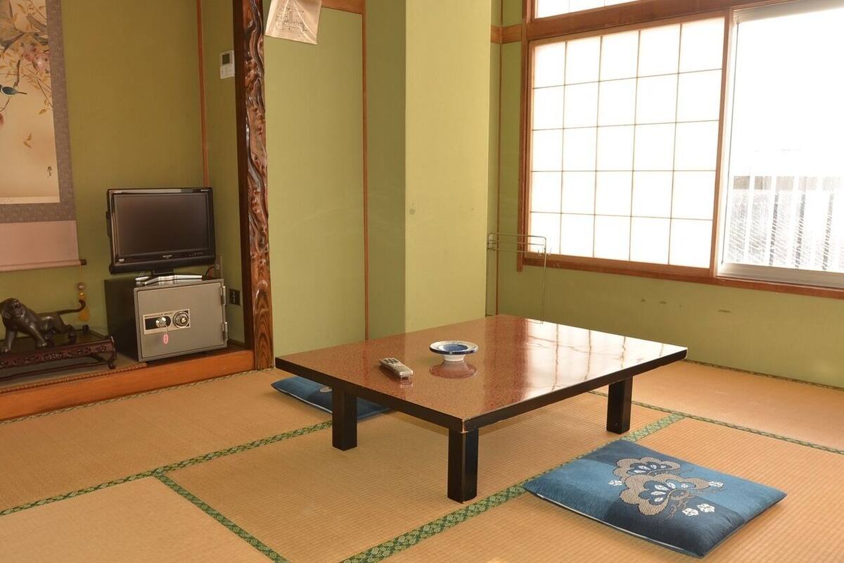 Une pièce avec un sol recouvert de tatamis, une petite table basse, un téléviseur et une statue de lion décorative.