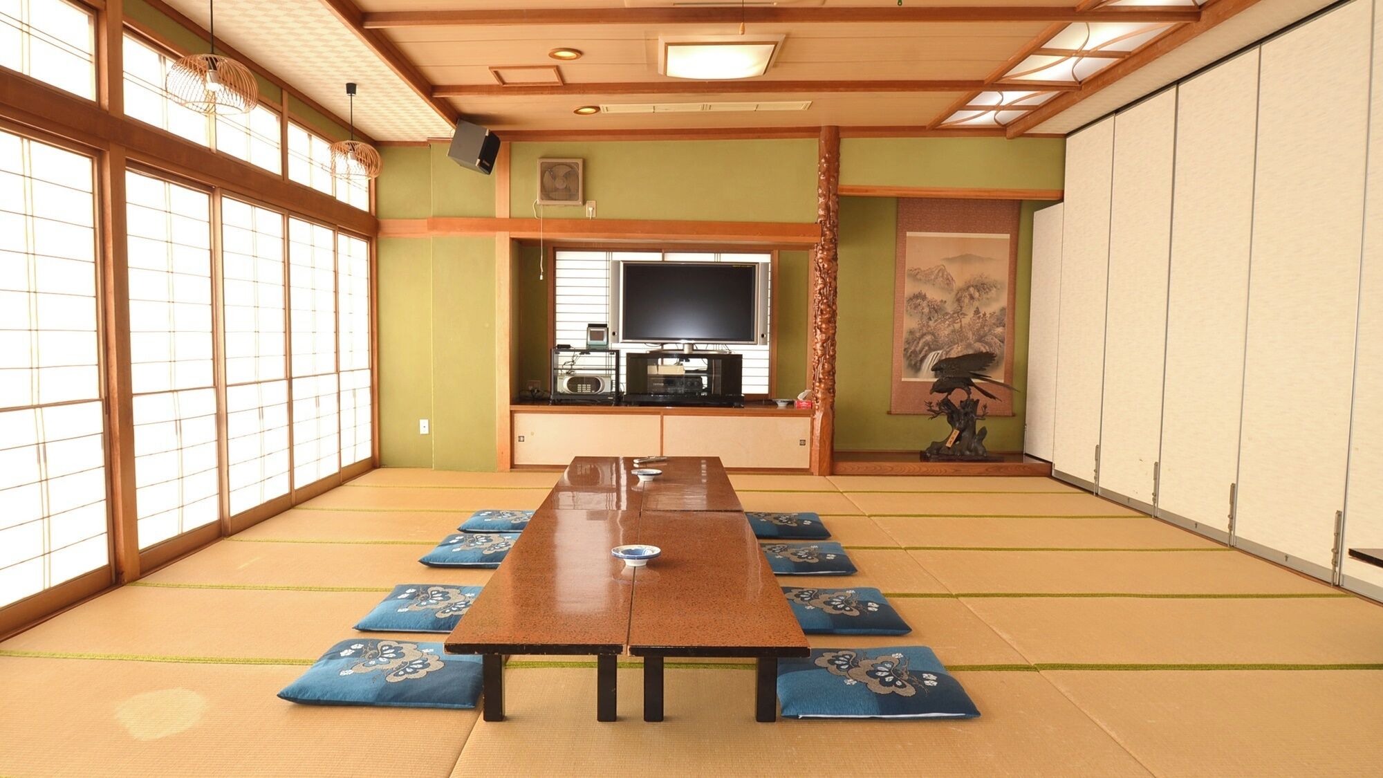 A tatami mat room with a long table, sliding doors, and a television.
