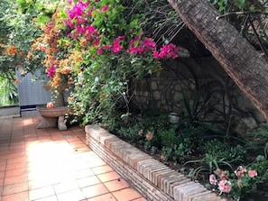 Ein Garten mit einem Ziegelpflanzkübel, einer Steinsäule und blühenden Pflanzen.
