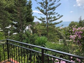 Ein Balkon mit Geländer, umgeben von üppiger Vegetation und Blick aufs Meer.