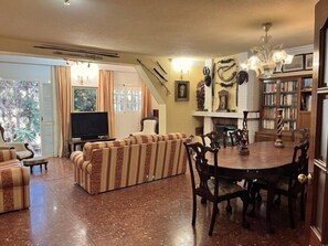 A living room with a sofa, a dining table, chairs, a television, and a fireplace.