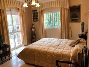 A bedroom with a large bed, a chandelier, a dresser, and a window with curtains.