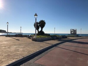 Eine gepflasterte Promenade mit Bänken, Straßenlaternen und einer Palme.