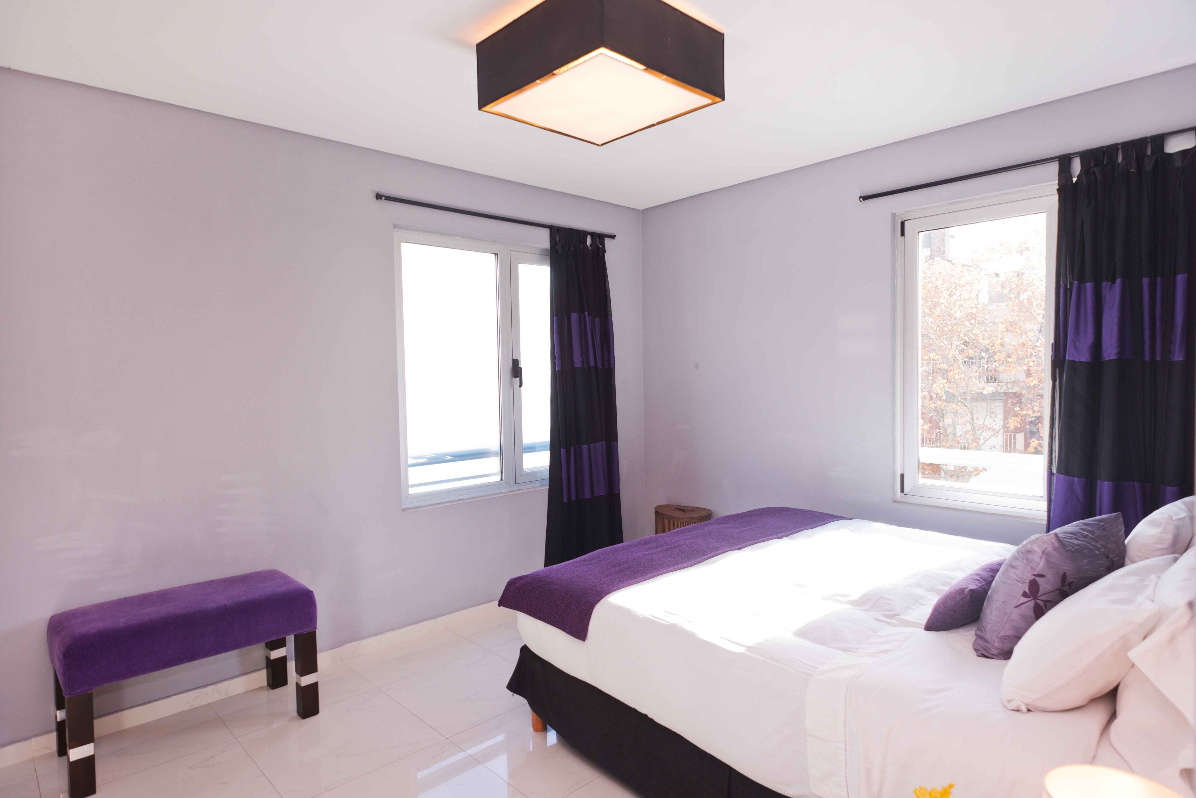 A modern bedroom with a large bed, a bench, and a window with curtains.