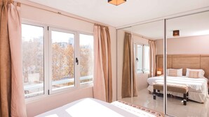 A hotel room with a large bed, a glass partition, and a view of autumn trees.