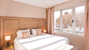 A hotel room with a large bed, a headboard, two bedside lamps, and a window with curtains.