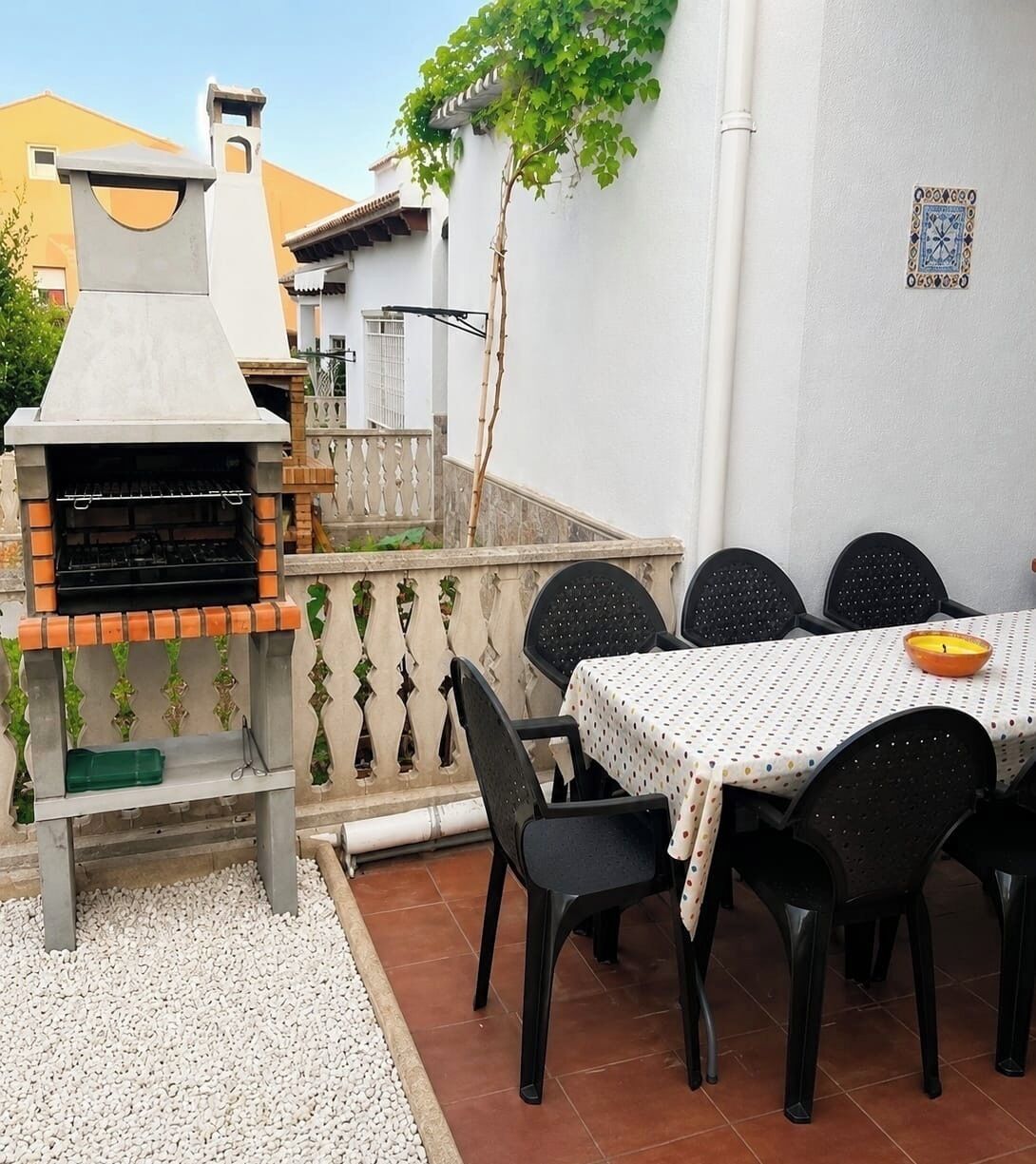 An outdoor patio with a barbecue grill, a table with chairs, and a decorative wall.