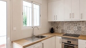 A modern kitchen with white cabinetry, a dishwasher, an oven, and a window providing natural light. - House on the beach between Barcelona and Tarragona (Torredembarra)