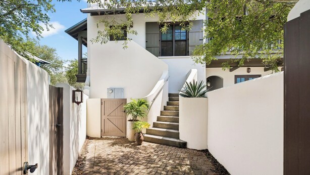 A modern house with a curved staircase leading to a second floor, surrounded by white walls and a wooden fence. - Carriage House | 30 Sec Walk to Beach | Pool Access | Across Eastern Green (Rosemary Beach)