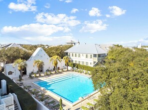 A pool area with lounge chairs, a white building with a triangular roof, and a large house with a grey roof. - Carriage House | 30 Sec Walk to Beach | Pool Access | Across Eastern Green (Rosemary Beach)