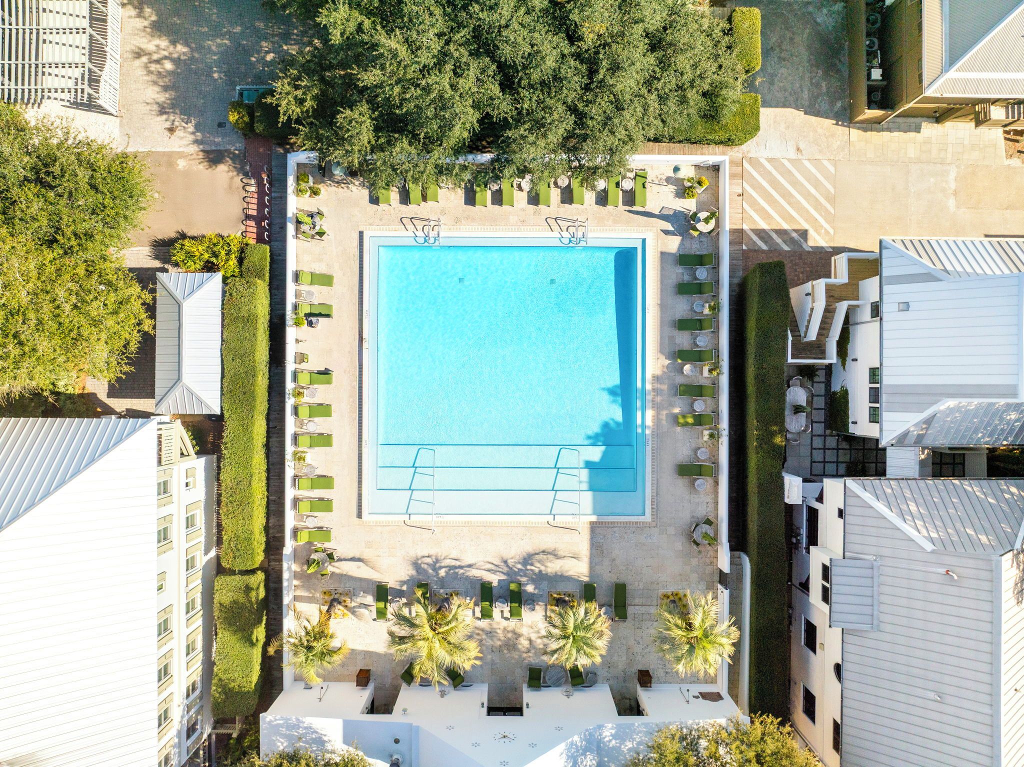 An aerial view of a hotel with a central swimming pool, surrounded by lounge areas and greenery.