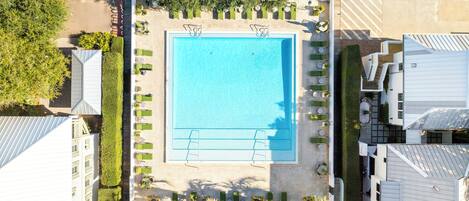 An aerial view of a hotel with a central swimming pool, surrounded by lounge areas and greenery.